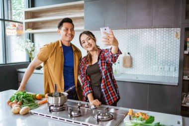 Asyalı çift mutfakta birlikte yemek yaparken selfie çekiyor.