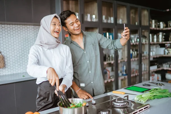 Casal muçulmano cozinhar sua comida na cozinha e tirar selfie — Fotografia de Stock