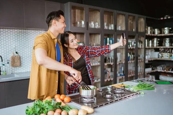 Ασιατικό ζευγάρι βγάζει selfie ενώ μαγειρεύουν μαζί στην κουζίνα — Φωτογραφία Αρχείου