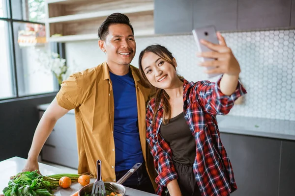 Asiático casal tomando selfie enquanto cozinhar juntos na cozinha — Fotografia de Stock