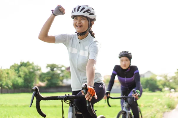 Mujer joven emocionada montando su bicicleta de carretera con un amigo — Foto de Stock