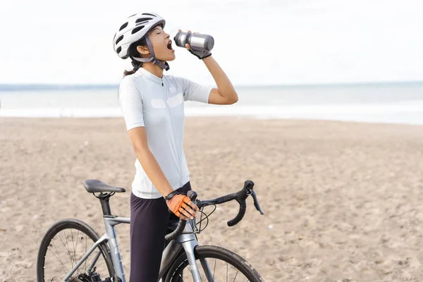 Ciclista femenina que tiene una botella de agua en la playa — Foto de Stock