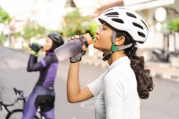 Женщина-велосипедистка с бутылкой воды на обочине дороги — стоковое фото