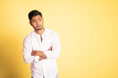 Elleri çaprazlanmış, sıkılmış yüzlü Asyalı genç adam.