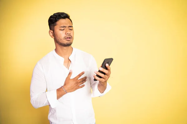 Mladý asijský muž šokován při sledování videa pomocí mobilního telefonu — Stock fotografie