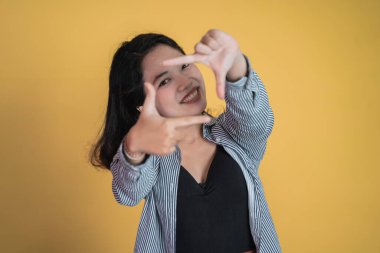 Bir çerçeve oluşturan parmaklar arasından bakan genç bir kadın