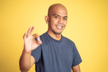 Dişlerini göstererek gülümseyerek el hareketi yapan kel bir adam.