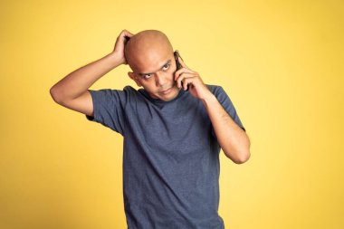 Üzgün Asyalı kel adam telefonu dinlerken kafasını kaşıyordu.