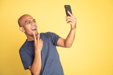 Kel ve barış yanlısı bir adam telefon kamerasıyla selfie çekiyor.