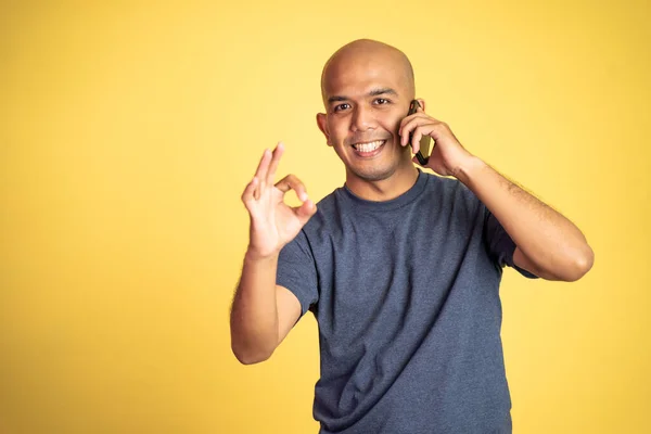 Šťastný asijský plešatý muž ukazuje v pořádku gesto dělat telefonát — Stock fotografie