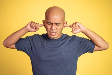 Kel adam rahatsız edici bir ifadeyle parmakları kulaklarını kapatıyor.