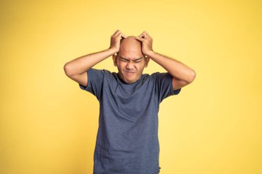 Stresli Asyalı kel genç adam başını tutuyor.