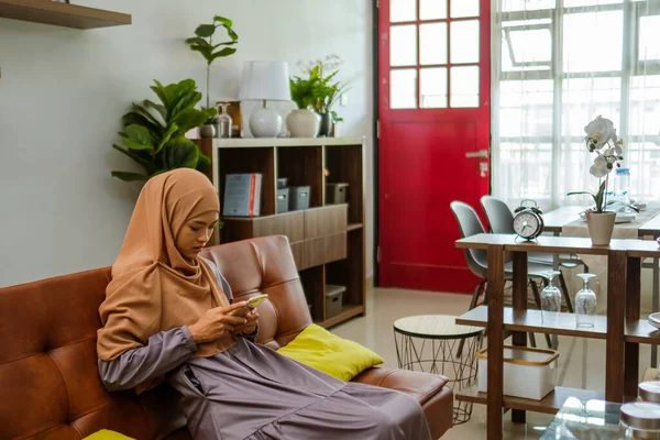 Muslim žena sedí na pohovce pomocí svého mobilního telefonu — Stock fotografie