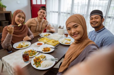 Asyalı Müslüman arkadaş iftar yemeği yerken akıllı telefonla selfie çekiyor.