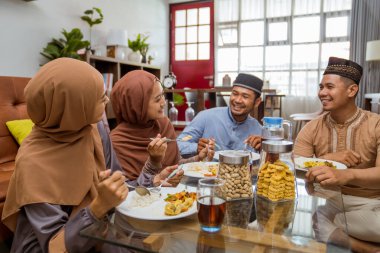 Arkadaş, oturma odasında yerde otururken birlikte iftar yemeği yiyor.