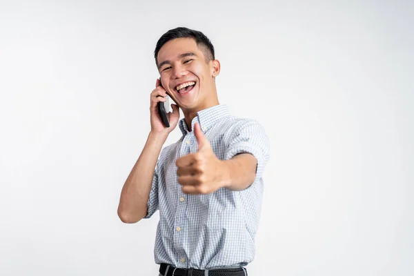 Szczęśliwy młody człowiek pokazuje kciuki do góry podczas słuchania telefonu komórkowego — Zdjęcie stockowe