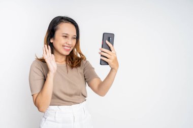 Kadın cep telefonuyla merhaba işareti yaparak bir video görüşmesi yapıyor.