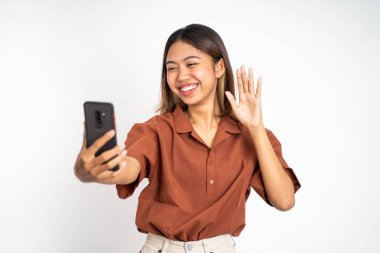 Kadın cep telefonuyla merhaba işareti yaparak bir video görüşmesi yapıyor.