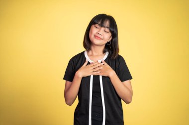 Arka planda rahatlamış hissederken göğsünü tutan genç bir kadın.