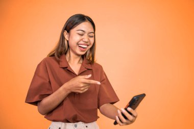 Heyecanlı Asyalı kadın cep telefonunu işaret ederek gülüyor