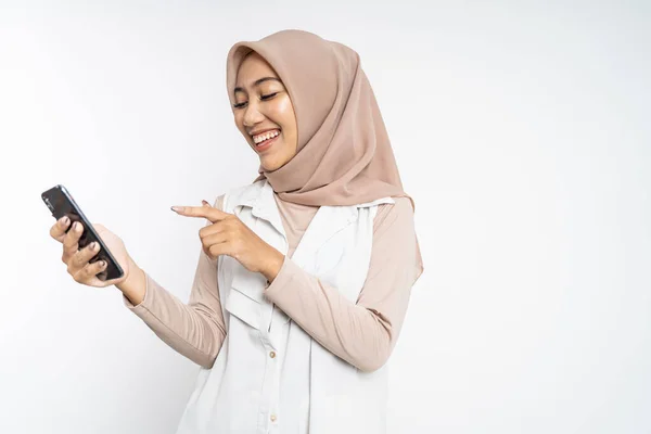 Мусульманская женщина смеется пальцем, указывая на свой мобильный телефон — стоковое фото