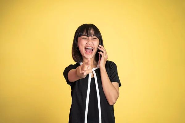 Збуджена азіатська жінка сміється з пальцем, вказуючи на її мобільний телефон — стокове фото