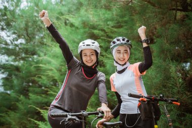 İki peçeli kadın bisiklet sürerken yumruklarını sıkmış gülümsüyor.