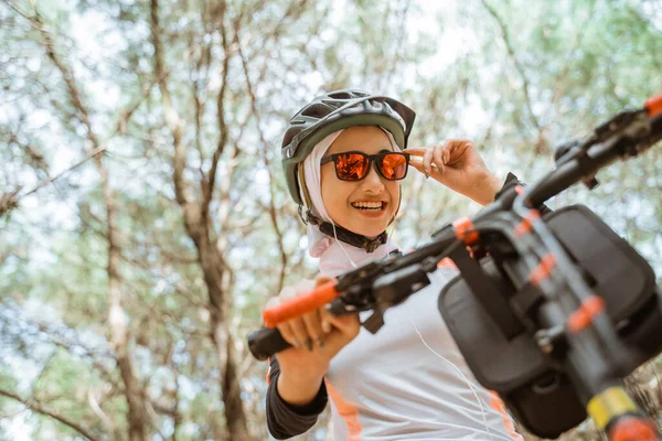 Závoj asijské dívka drží sluneční brýle s úsměvem při jízdě na kole v parku — Stock fotografie