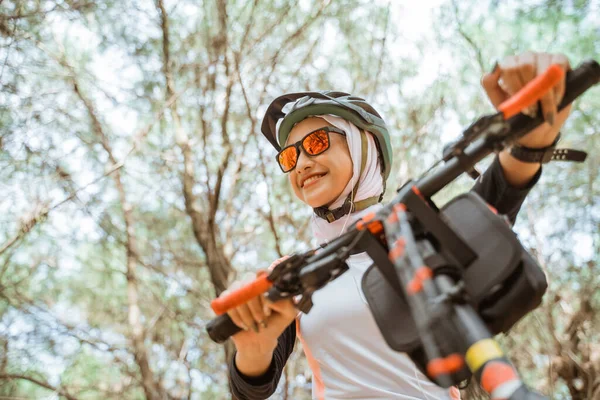 Menina de véu atraente em óculos de sol sorrindo enquanto pedalava no parque — Fotografia de Stock