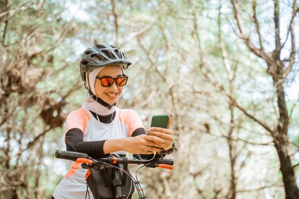 Mujer con velo en gafas de sol usando el teléfono celular mientras pedalea en el parque — Foto de Stock