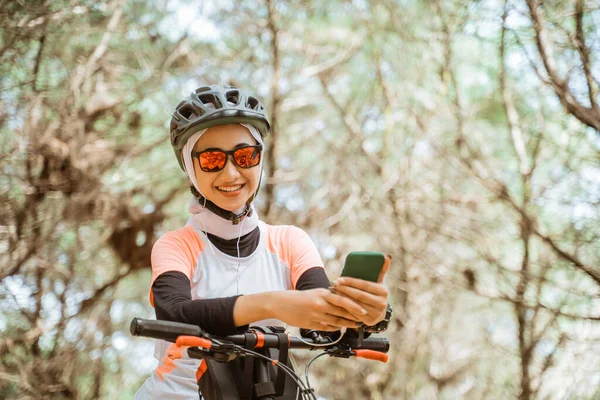 Chica con velo en gafas de sol usando el teléfono celular mientras pedalea en el parque — Foto de Stock
