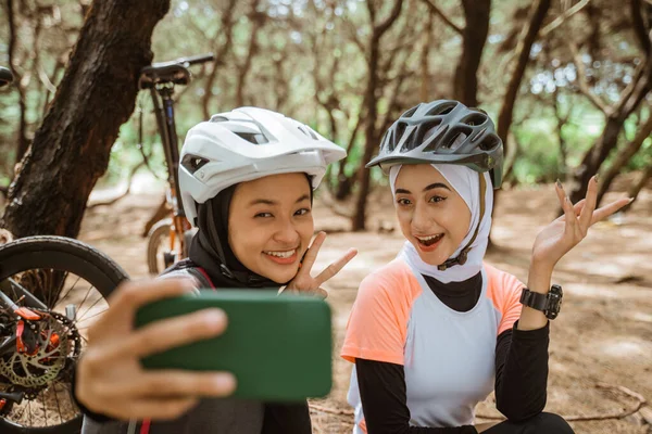 Dvě zahalené dívky selfie pomocí mobilů při jízdě na kole — Stock fotografie