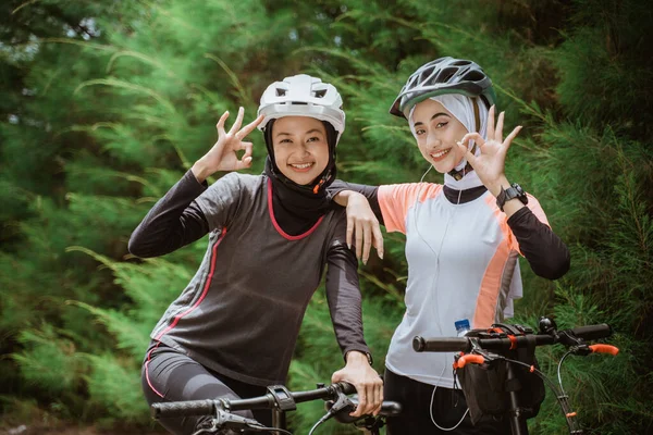 Dvě zahalené ženy s úsměvem v pořádku gesto ruky při jízdě na kole — Stock fotografie