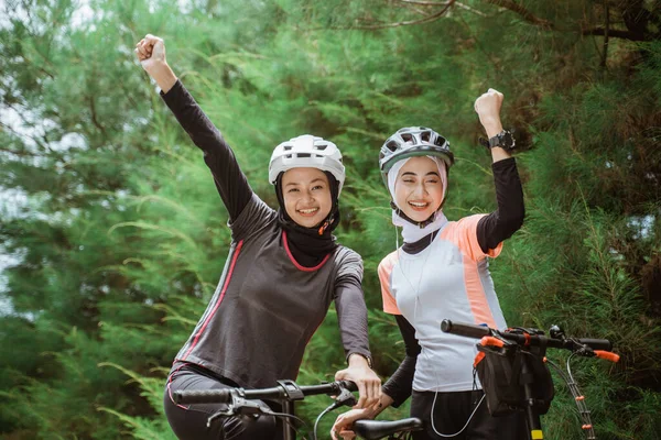 İki peçeli kadın bisiklet sürerken yumruklarını sıkmış gülümsüyor.