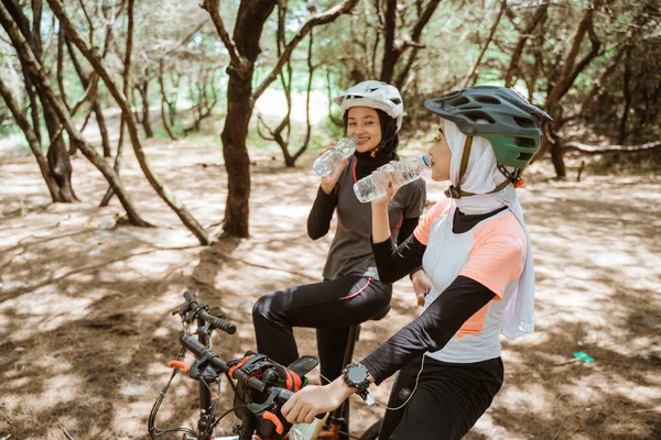 Dvě mladé muslimky pití minerální vody láhve při jízdě na kole — Stock fotografie