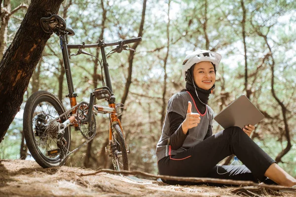 Zahalená dívka sedí ve sluchátkách s palci nahoru při jízdě na kole — Stock fotografie