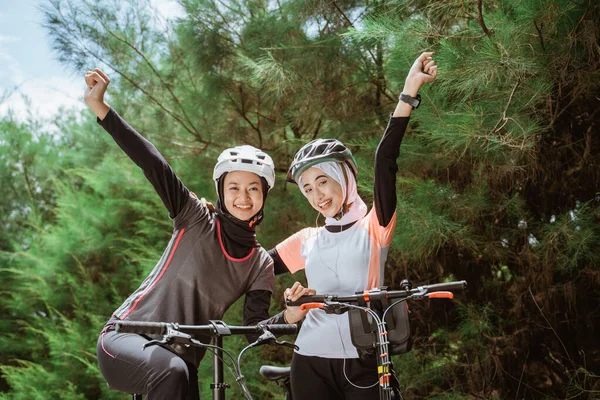 Radost ze dvou zahalených dívek se zaťatými pěstmi při jízdě na kole — Stock fotografie