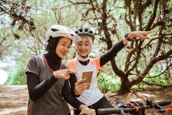 Dos mujeres musulmanas usando un teléfono móvil mientras pedalean — Foto de Stock
