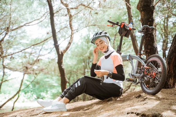 Otururken ve dinlenirken kulaklık ve tablet kullanan peçeli kadın.