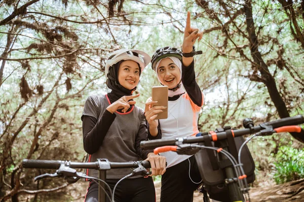 Dvě ženy na kole pomocí mobilního telefonu ukazuje na silnici — Stock fotografie