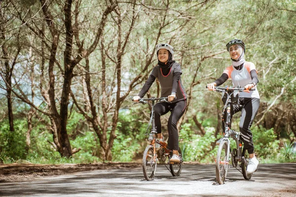Two attractive Muslim women enjoying cycling together on the road — стоковое фото