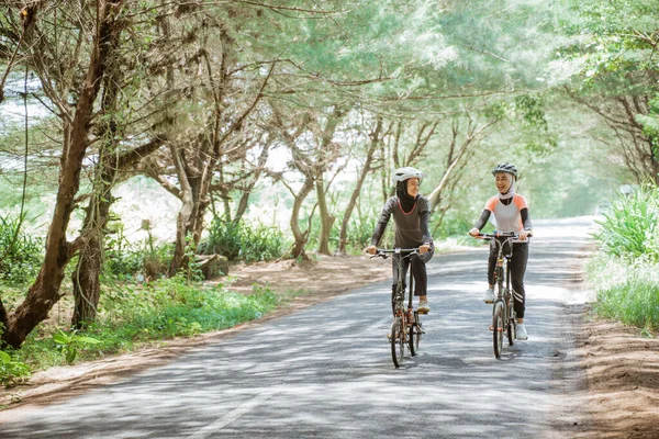 Two asian muslim women enjoying cycling together on the street — Stock Fotó