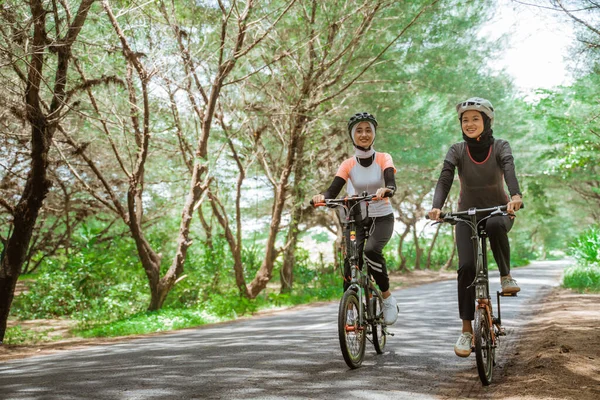 Two women cycling on a road with lots of trees — Stock Fotó