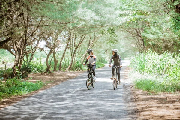 Two muslim women cycling on the road many trees background — ストック写真