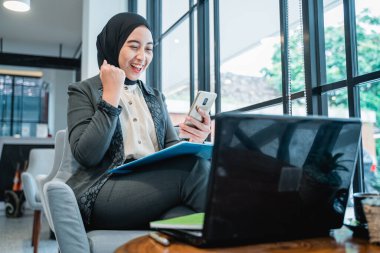 Heyecanlı Müslüman kadın telefonuna bakarken kolunu kaldırıyor.