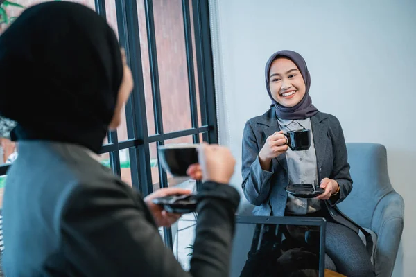 Dois asiático muçulmano mulher falando enquanto sentado no um sofá apreciando café — Fotografia de Stock