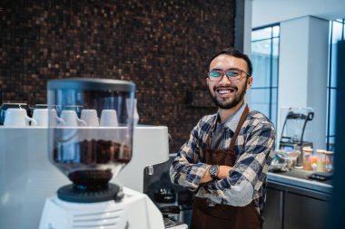 Kahve dükkanının önünde elleri çapraz duran barmen.