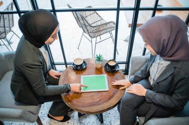 Müslüman kadın işçi meslektaşıyla tablet kullanarak tartışıyor.