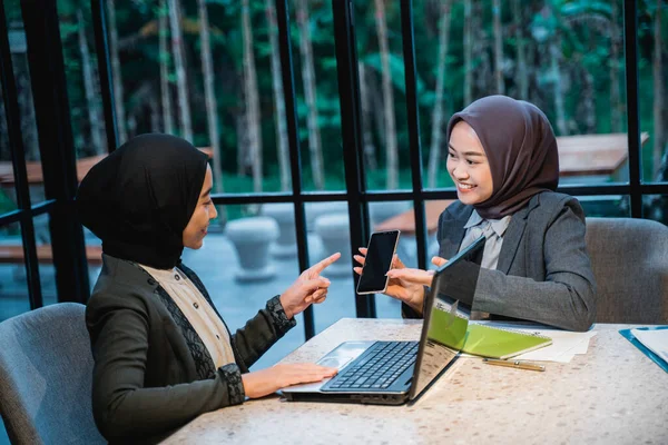 woman with hijab showing her phone to his friend while working