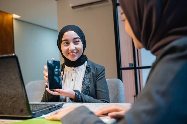 Woman with hijab showing her phone to his friend while working — Fotografia de Stock